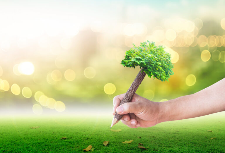 Ruka drži olovku dizajniranu kao drvo, sa zelenom krošnjom i pozadinom od trave