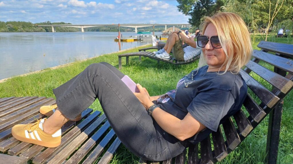 Žena u opuštenoj pozi, na drvenoj klupa ležaljci, u izletištu Obrenovca, posmatra reku