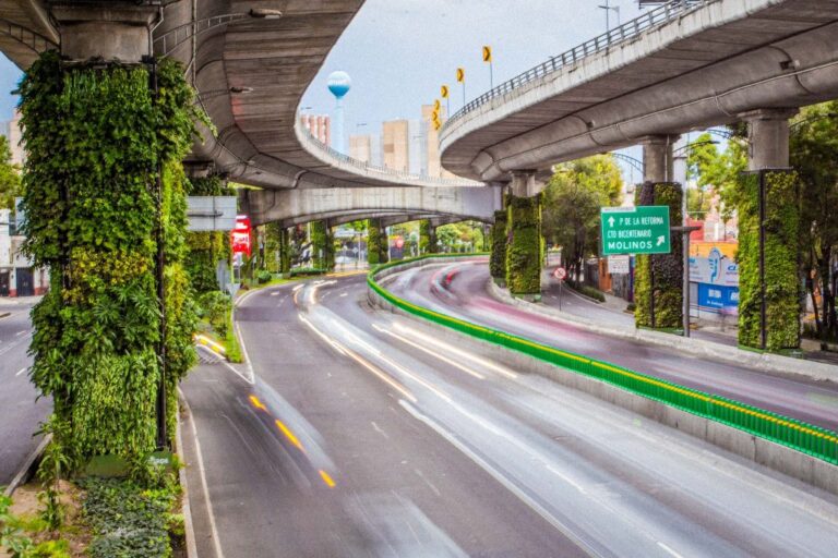 Višespratni gradski autoput sa vertikalnim vrtovima na stubovima, uz svetlosne tragove vozila u pokretu.