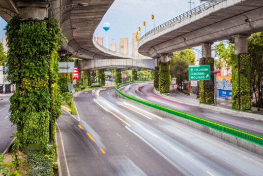 Višespratni gradski autoput sa vertikalnim vrtovima na stubovima, uz svetlosne tragove vozila u pokretu.