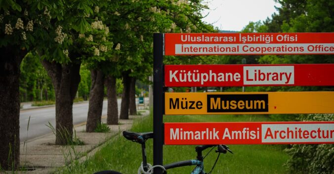 A bicycle parked on grass beside a multilingual sign in Ankara, Turkey.
