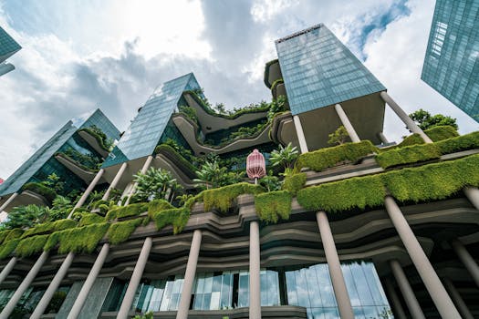 pogled iz žablje perspektive na staklenu zgradu sa ozelenjenom fasadom, sa ogromim belim oblacima na nebu