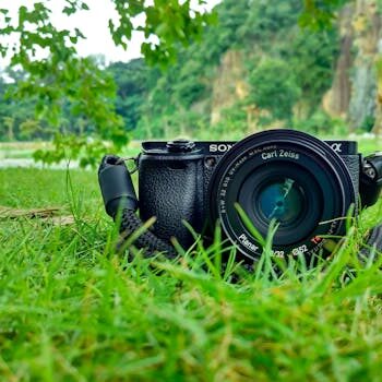 Camera with Carl Zeiss lens on grass, surrounded by nature and vibrant greenery.