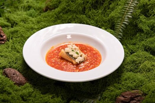 Colorful gourmet dish with crispy topping served on a white plate over lush green moss.