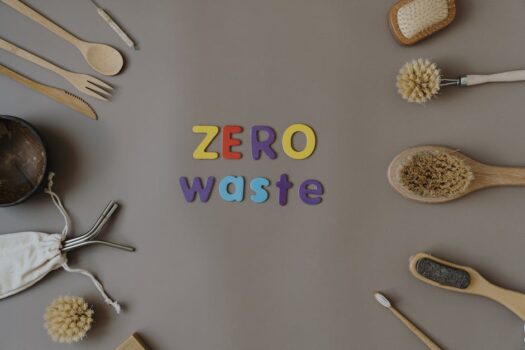 Drveni pribor za kuhinju i ličnu negu, poređan u krug po stolu na kome šarenim slovima piše Zero waste