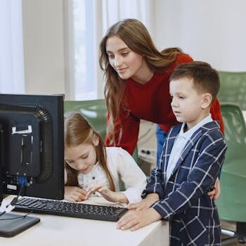 Učiteljica pokazuje dečaku i devojčici nešto na računaru u učionici.