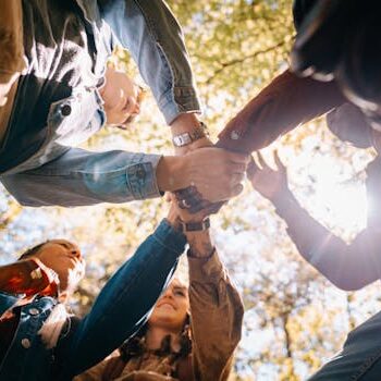 Raznolika grupa odraslih koji se drže za ruke u jedinstvu i prijateljstvu pod dnevnim svetlom.