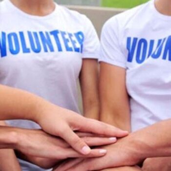 Osobe u belim majicama na kojima piše volonter ukrstile su ruke u pozdrav zajedništva